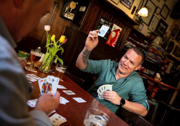 Man die een kaartspel speelt en een bier drinkt op café. 
