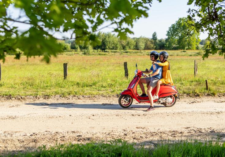Een koppel zit op een rode vespa